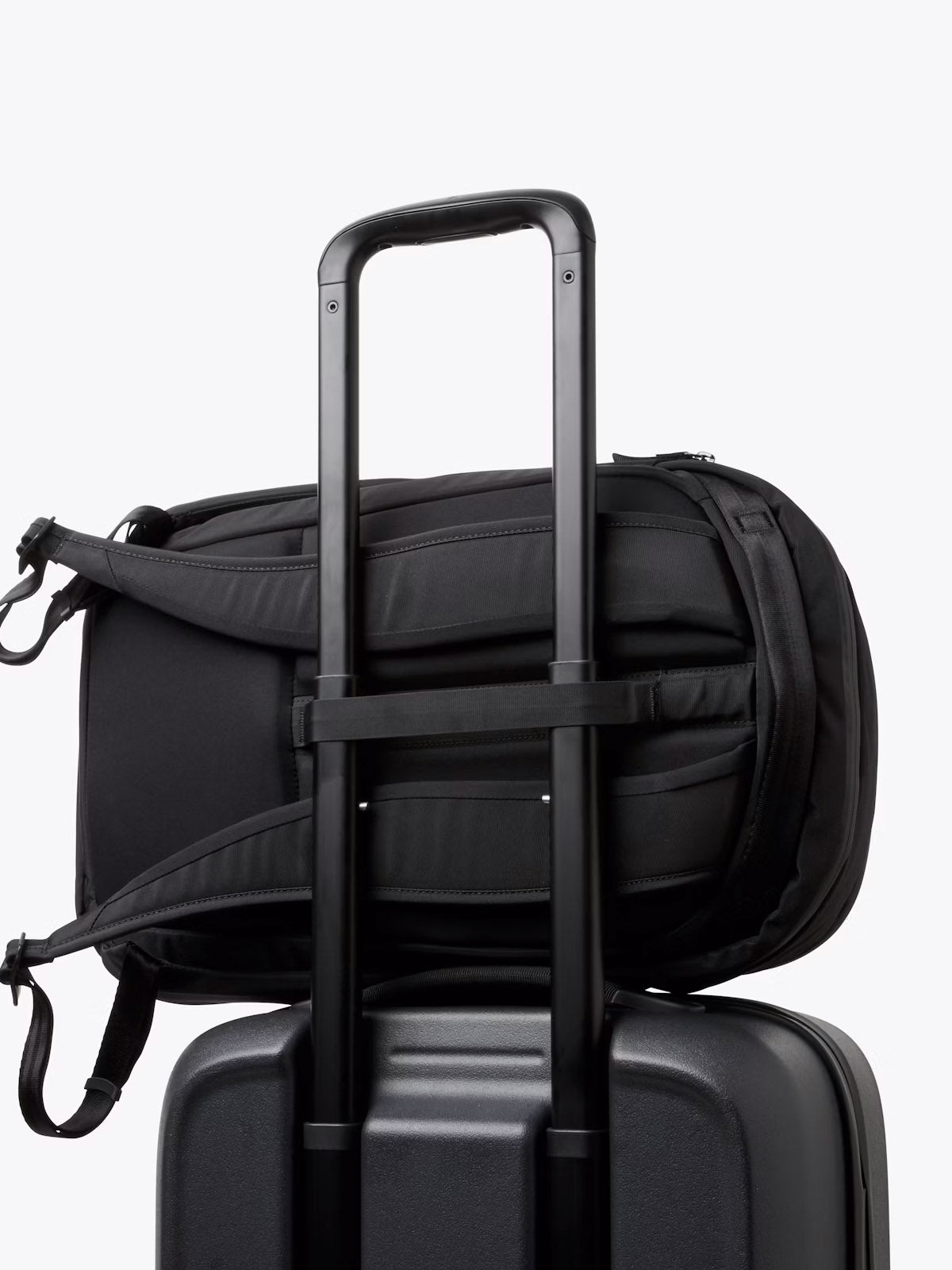 The Bellroy Transit Workpack - 20L, a sleek black backpack with a laptop sleeve, is attached to the handle of a hard-shell suitcase, illustrating a smart travel setup against a plain white background.