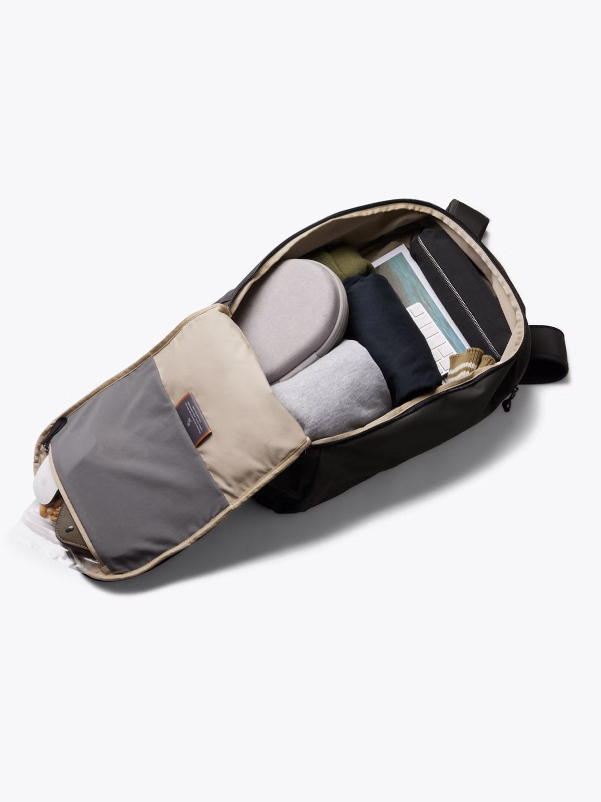 The Bellroy Transit Workpack - 20L in black is open, revealing neatly packed clothes, shoes, a water bottle in the side pocket, a front-flap zippered pouch for organization, and a dedicated laptop sleeve.