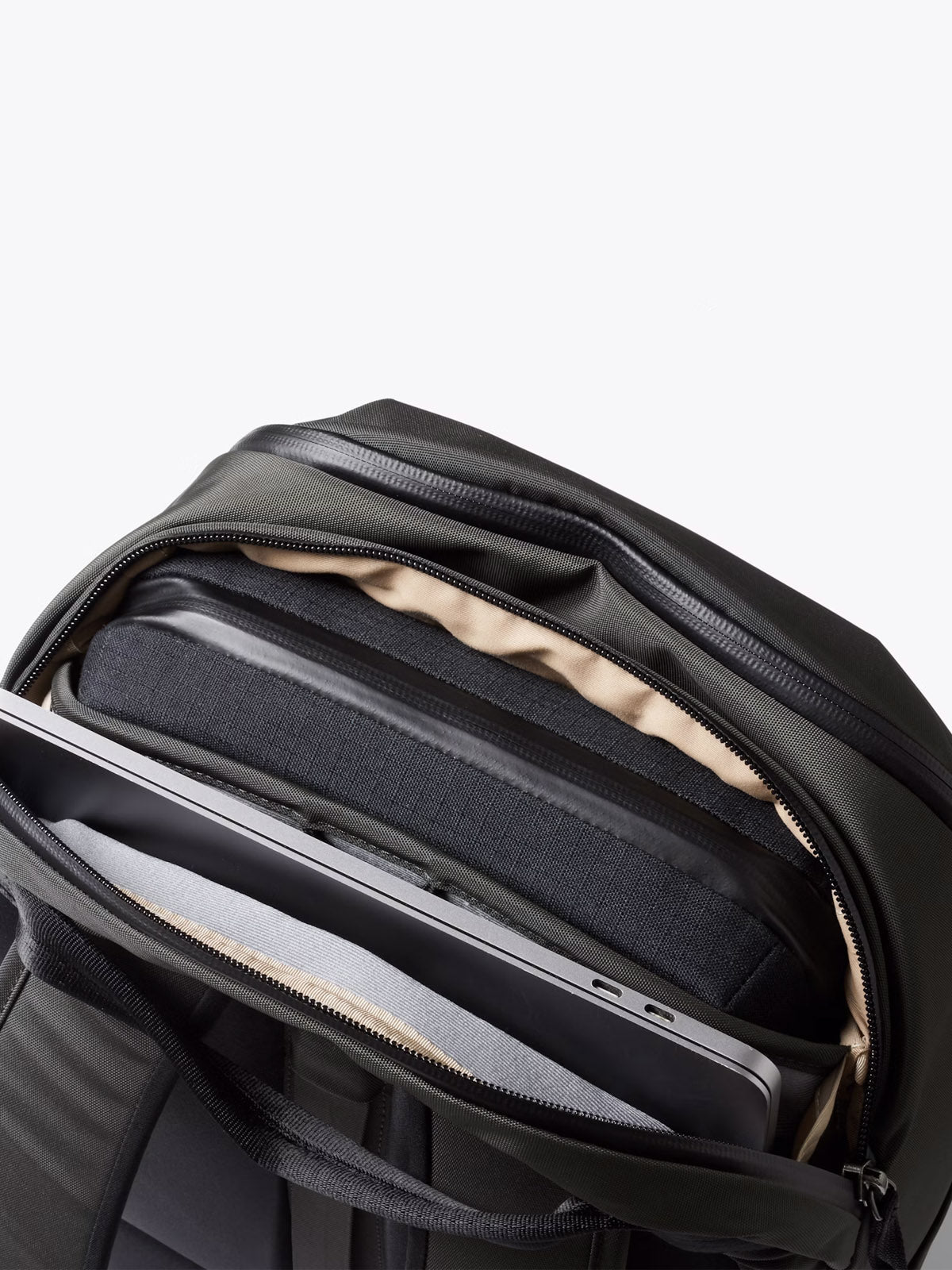 The Bellroy Transit Workpack - 20L in dark green features a minimalist design with a beige interior, dedicated laptop sleeve, and organized compartments, all revealed through partially unzipped zippers displaying your electronics and accessories.