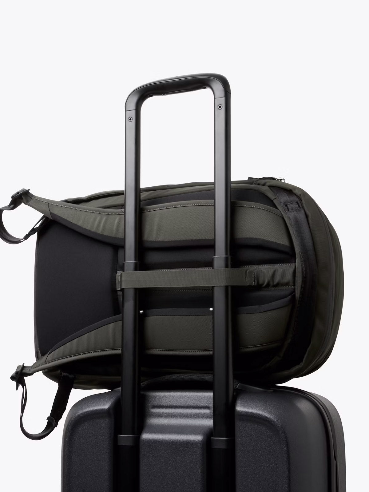 The Bellroy Transit Workpack - 20L, a minimalist black work bag, is secured atop a black suitcase with its strap looped over the handle, set against a plain white background.