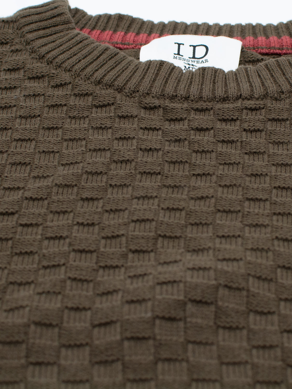 Close-up of the Turku Cotton Sweater by ID Menswear, showcasing a brown textured knit with a subtle grid design. The label reads ID Menswear M for a regular fit. A hint of red fabric inside the collar provides contrast to this checked cotton sweater.