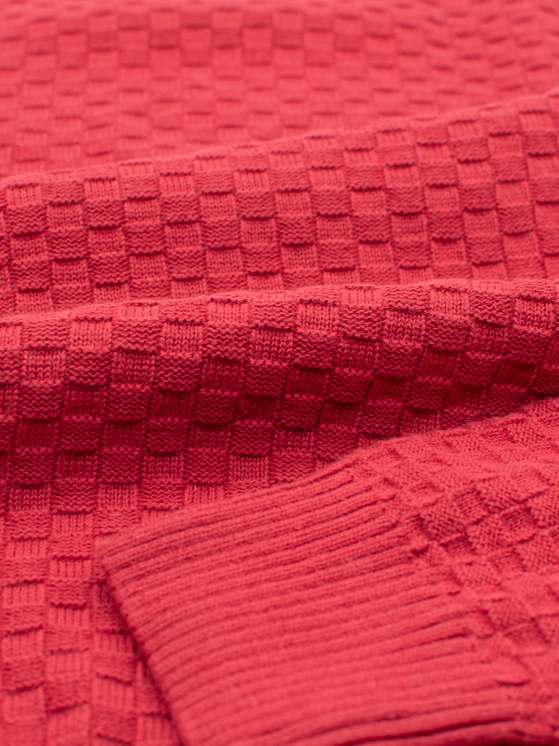 Close-up of the ID Menswear Turku Cotton Sweater featuring a stylish red checked knit pattern. The visible sleeve showcases a ribbed cuff, highlighting the intricate texture of its regular fit fabric.