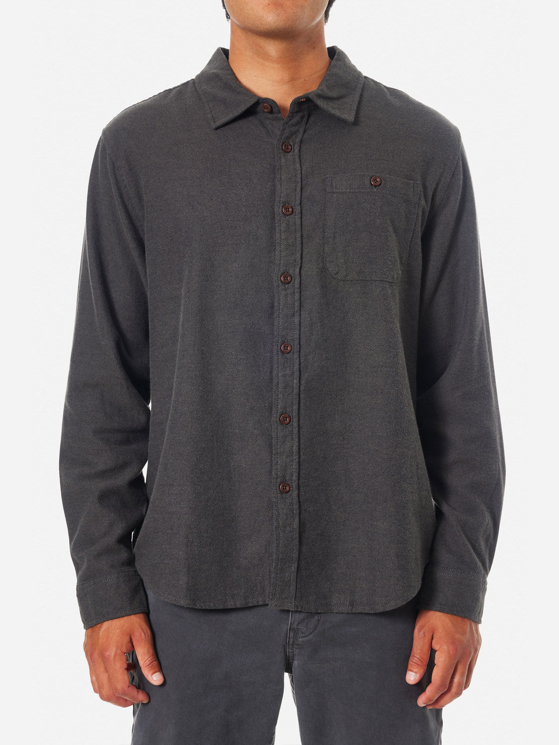 A person stands against a white background wearing a Katin Twiller Flannel Button Down Shirt in dark cotton, featuring a chest pocket, brown buttons, and an exquisite moleskin finish; their face remains unseen.