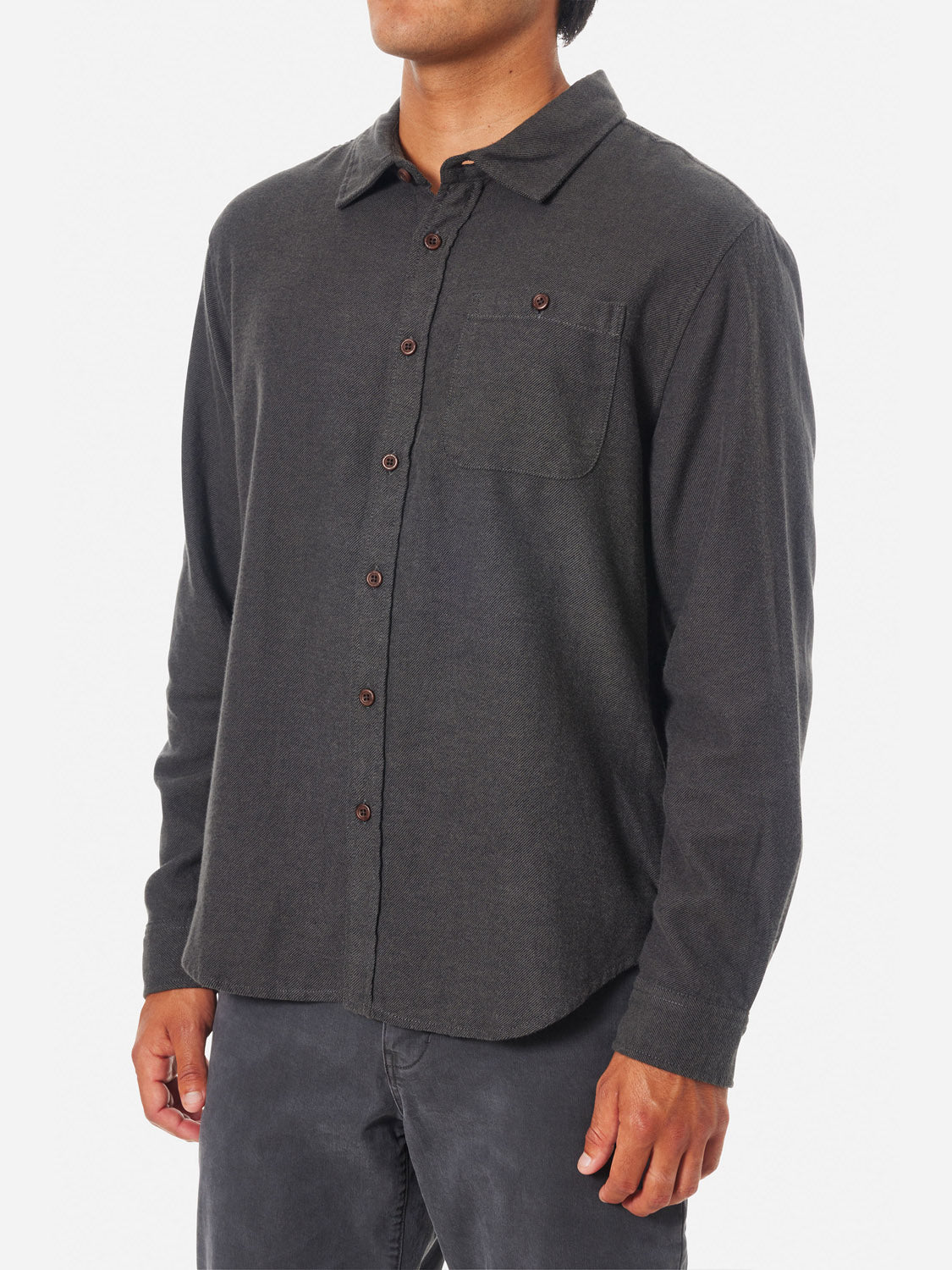 Someone is wearing a Katin Twiller Flannel Button Down Shirt in dark gray, featuring long sleeves, a moleskin finish, and a chest pocket. The shirt is casually untucked with unrolled sleeves against a plain white background.