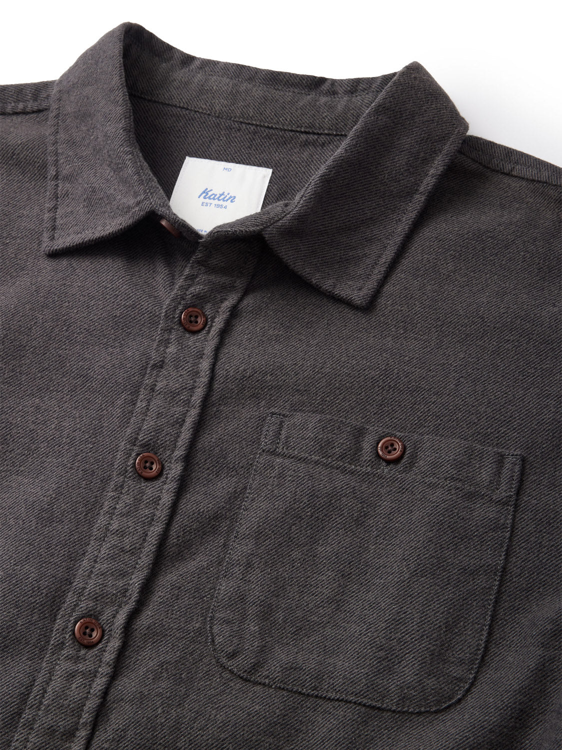 Close-up of the Katin Twiller Flannel Button Down Shirt in dark gray textured cotton flannel. It has brown buttons, a chest pocket, and an inside collar tag that is visible but not legible. The shirt is laid flat on a white surface.