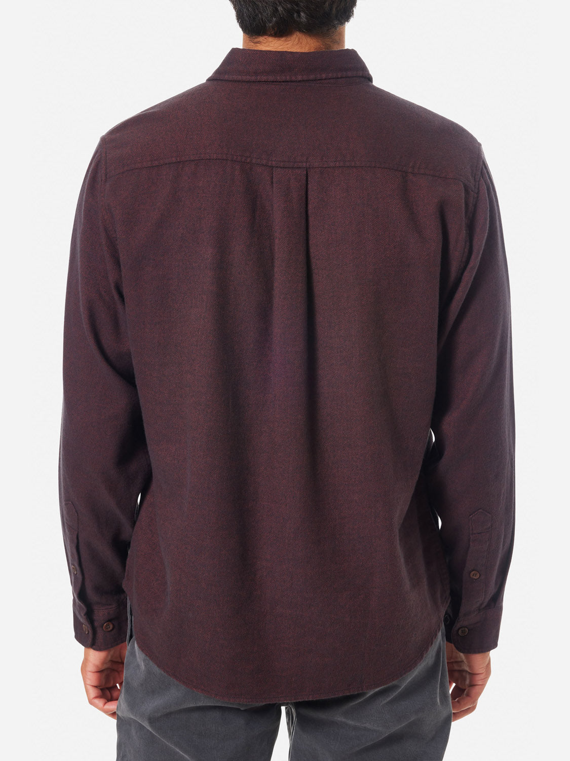 A person wearing the Katin Twiller Flannel Button Down Shirt, featuring a dark red hue and moleskin finish with buttoned cuffs, faces away from the camera. Complemented by dark pants, this ensemble contrasts strikingly against the plain white background.