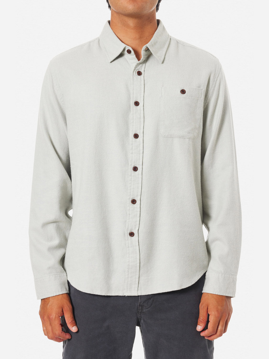 Against a white backdrop, someone wears the Katin Twiller Flannel Button Down Shirt in light gray, showcasing its cotton fabric, long sleeves, and front pocket. Their hands rest at their sides, complemented by dark pants.