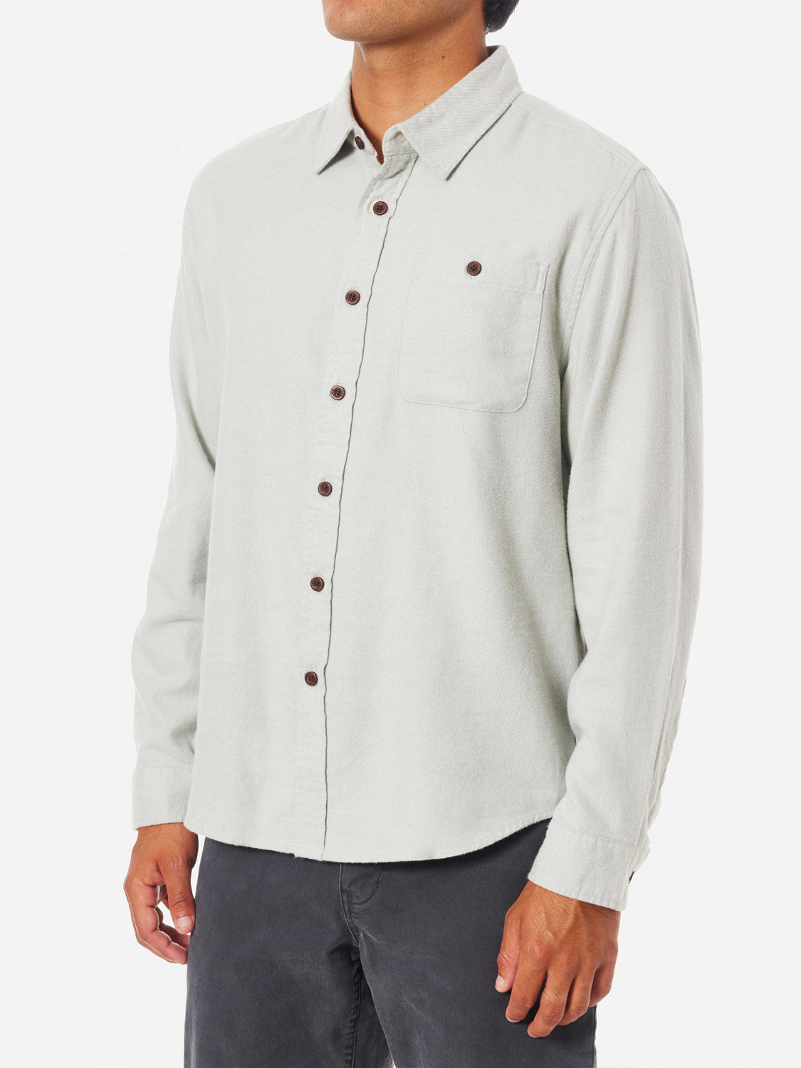 A man poses against a white backdrop in the Katin Twiller Flannel Button Down Shirt, featuring dark buttons and a front pocket on light grey 2-tone twill fabric. He pairs it with dark pants for a chic, understated style.