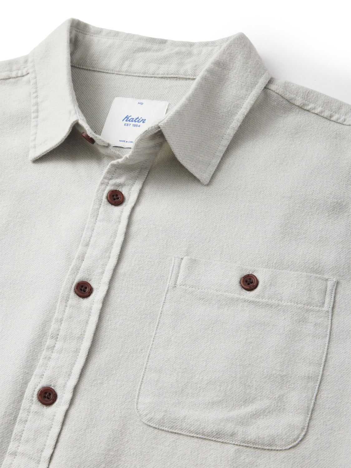 Close-up of the Katin Twiller Flannel Button Down Shirt, in light gray with brown buttons. Made from soft cotton flannel, it has a left front pocket and visible collar label. The textured fabric is enhanced by a subtle moleskin finish.