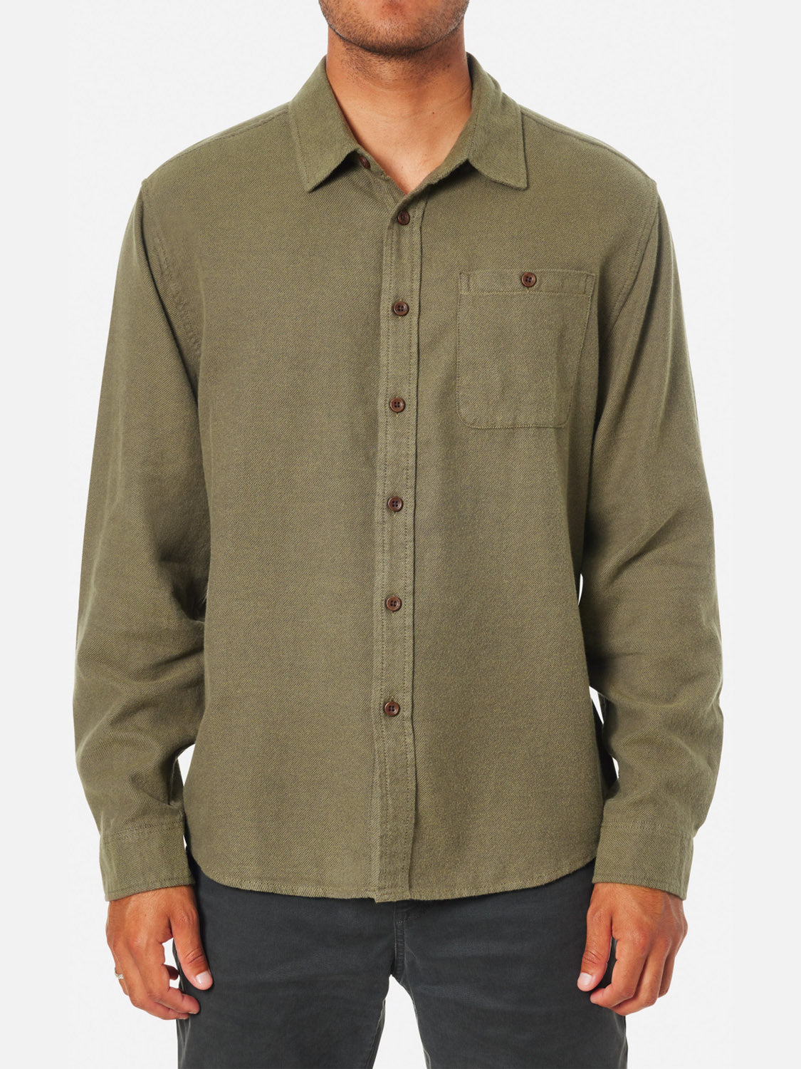 A person wearing a Katin Twiller Flannel Button Down Shirt in olive green, featuring long sleeves and a front chest pocket, stands against a plain white background. The face is not visible.
