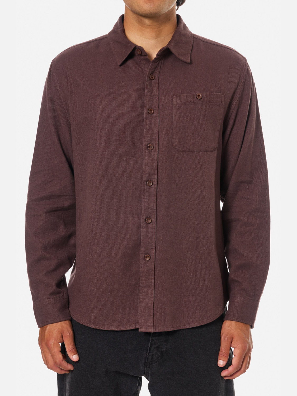 A man wears the Katin Twiller Flannel Button Down Shirt—a long-sleeve, dark brown, 100% cotton flannel shirt with a single chest pocket—standing against a plain white background.