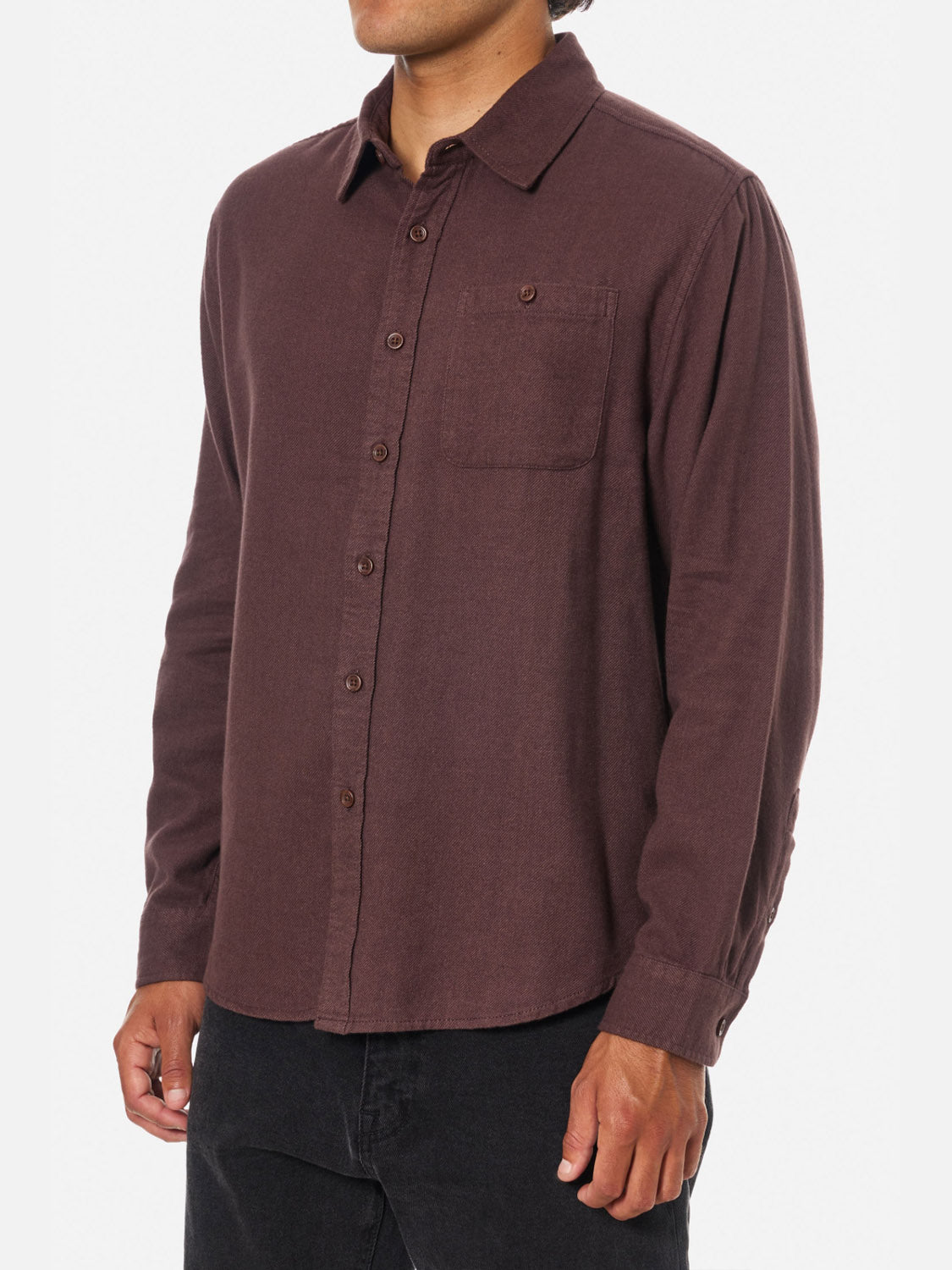 A person wearing the Katin Twiller Flannel Button Down Shirt—a long-sleeved, button-up dark brown 2-tone twill flannel with chest pocket—paired with black pants, standing against a plain white background.