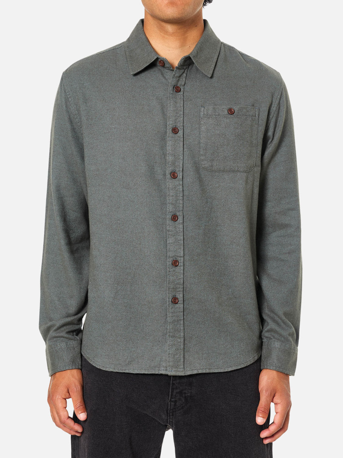A person wears the Katin Twiller Flannel Button Down Shirt—a long-sleeve, grayish-green cotton flannel with a chest pocket and dark buttons—paired with black pants, standing facing forward against a plain background.
