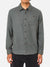 A person wears the Katin Twiller Flannel Button Down Shirt—a long-sleeve, grayish-green cotton flannel with a chest pocket and dark buttons—paired with black pants, standing facing forward against a plain background.