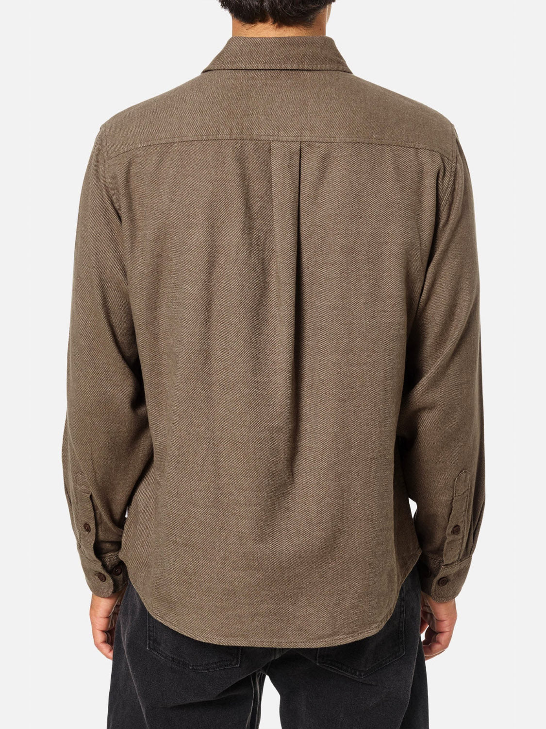 A person is seen from behind wearing the Katin Twiller Flannel Button Down Shirt, a long-sleeve brown cotton flannel with a back yoke and center pleat, paired with black pants, set against a plain white background.
