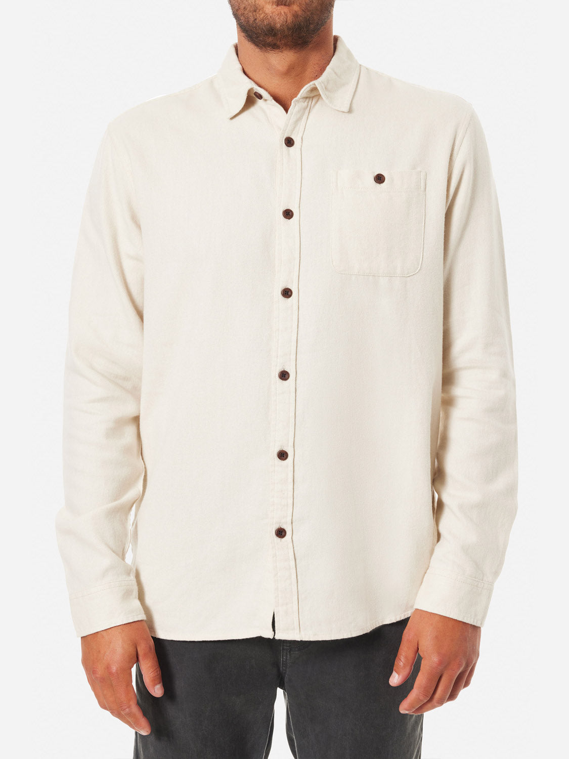 A person wears the Katin Twiller Flannel Button Down Shirt featuring a cream color, long sleeves, and a chest pocket with dark contrast buttons. The two-tone twill adds texture. They stand in dark pants with arms at their sides while their head isnt visible.