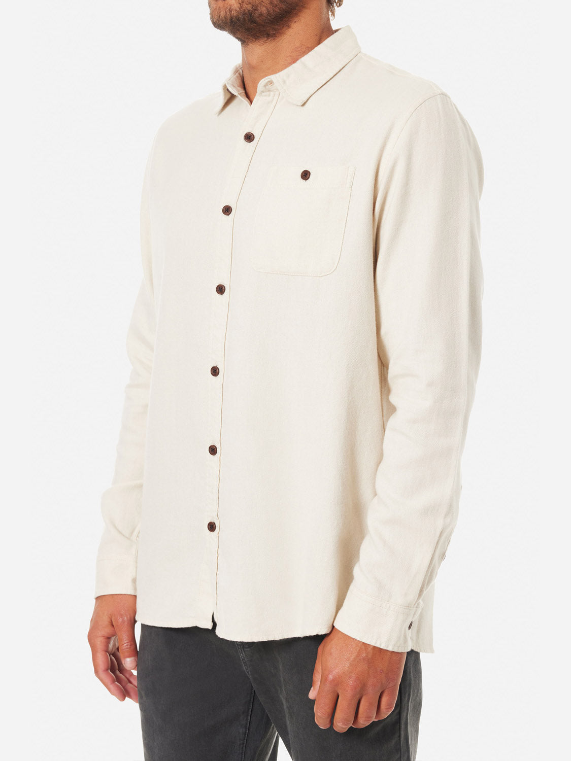 A person is wearing the Katin Twiller Flannel Button Down Shirt in cream with dark buttons and a left-side pocket, paired with dark pants. The shirt stands out against the plain white background.