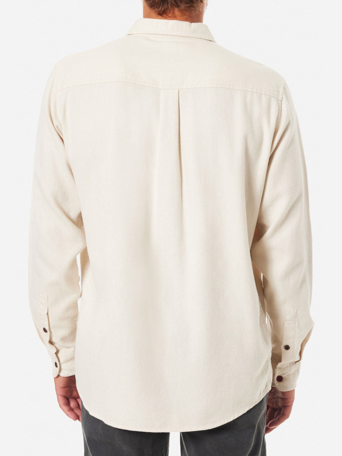 Seen from behind, a person wears the Katin Twiller Flannel Button Down Shirt in beige, showcasing its long sleeves and buttoned cuffs against a white background. Its paired stylishly with dark pants, exuding subtle sophistication.