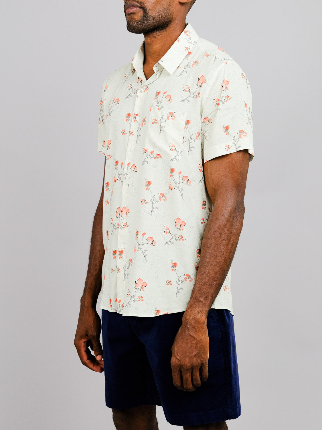 A man wears the Ume Printed Rayon Shirt by ID Menswear, featuring vibrant prints, paired with dark shorts, standing against a plain gray background.