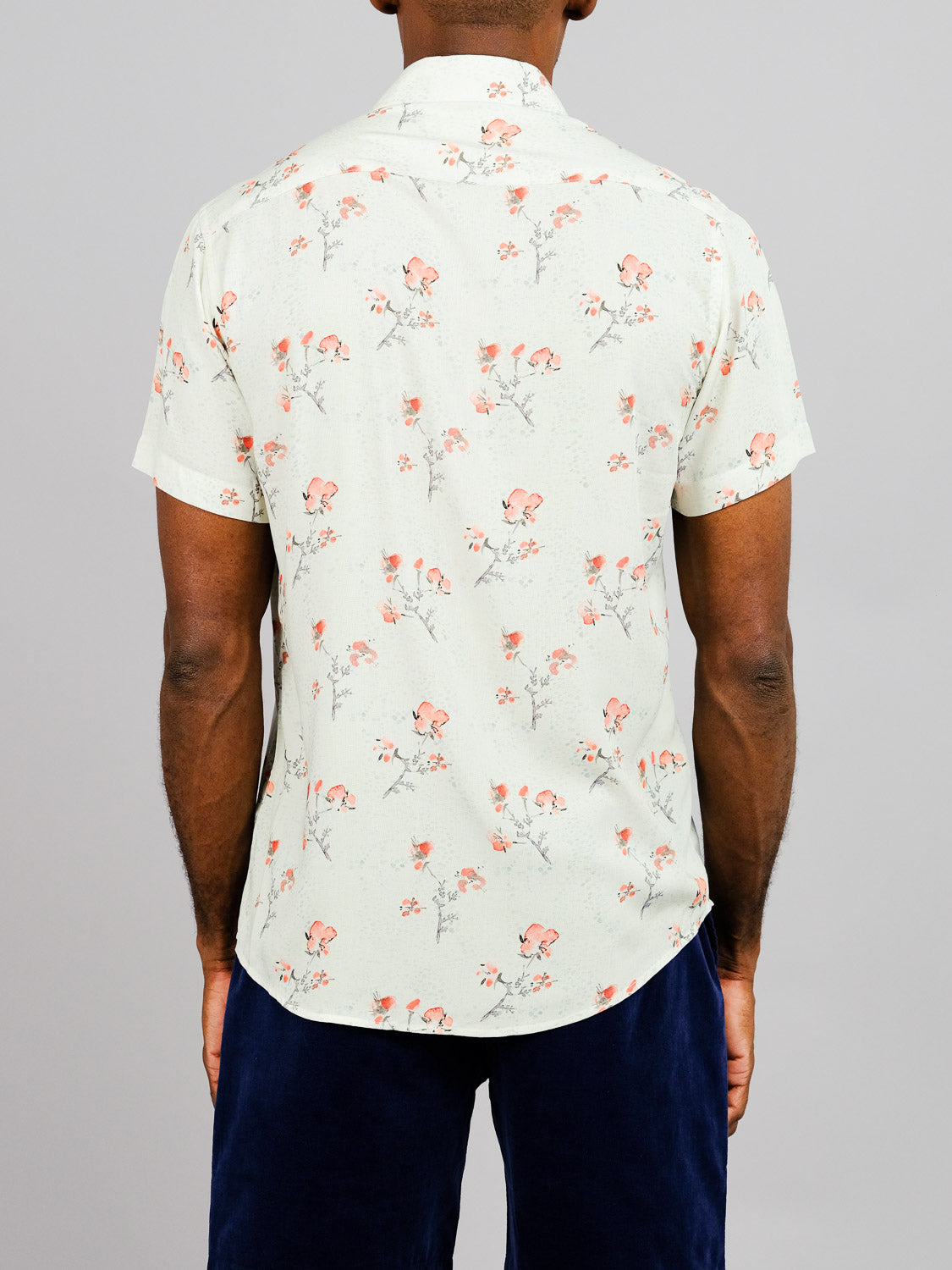A person stands facing away, wearing the ID Menswear Ume Printed Rayon Shirt with vibrant red floral prints and dark blue pants against a plain gray background.