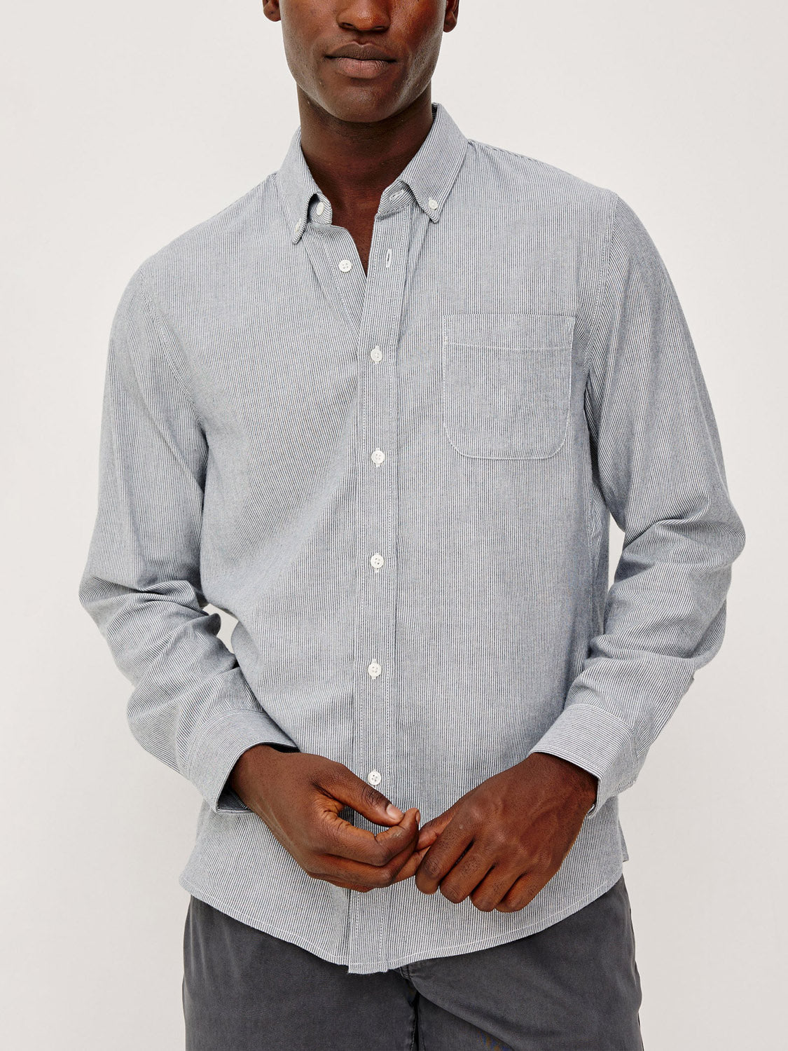 A person wears the Rails Vance Shirt—a light blue cotton-twill button-up with a chest pocket—paired with dark pants, standing against a plain background. Their face is partially visible, showcasing a classic everyday style.