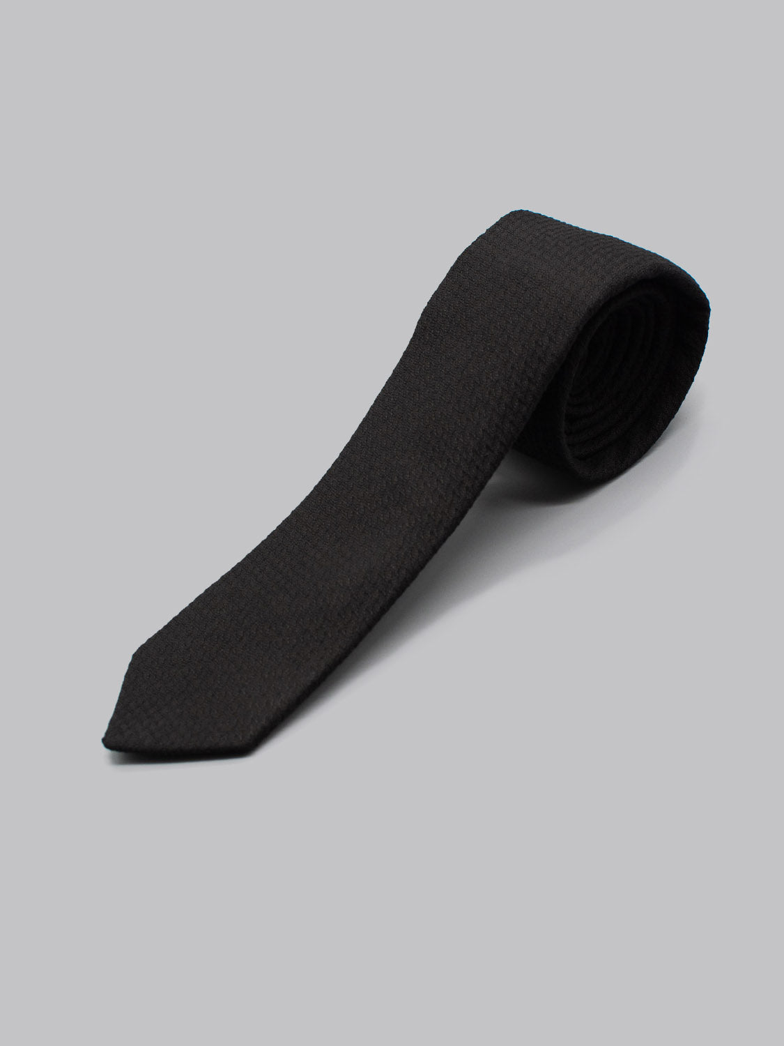 The ID Cotton Tie Venice by ID Menswear, a handmade black textured cotton tie, is neatly rolled and displayed on a plain light gray background.