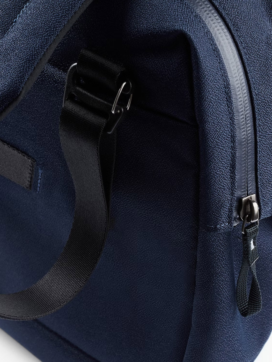 Close-up of the Bellroy Via Work Bag - 14L in navy blue, crafted from recycled fabric. Features include a black strap with metal buckle, a partially open zipper with fabric pull tab, textured surface, and visible seams.