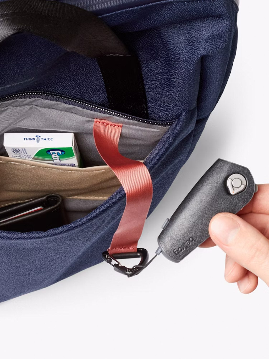 A hand pulls a retractable key holder attached to a red strap inside the Bellroy Via Workpack - 18L, a blue laptop backpack. Its pocket holds gum and a wallet, making this commuter bag practical and organized.