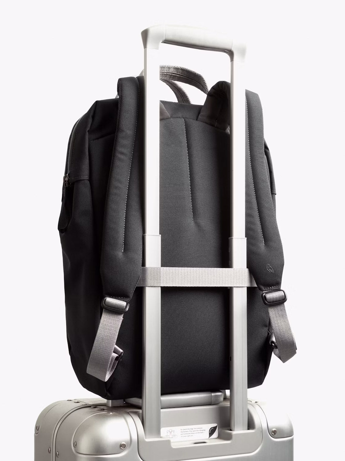 The Bellroy Via Workpack - 18L, a water-resistant laptop backpack, is securely attached to the handle of a silver rolling suitcase, with its straps and back panel visible against a plain white background.