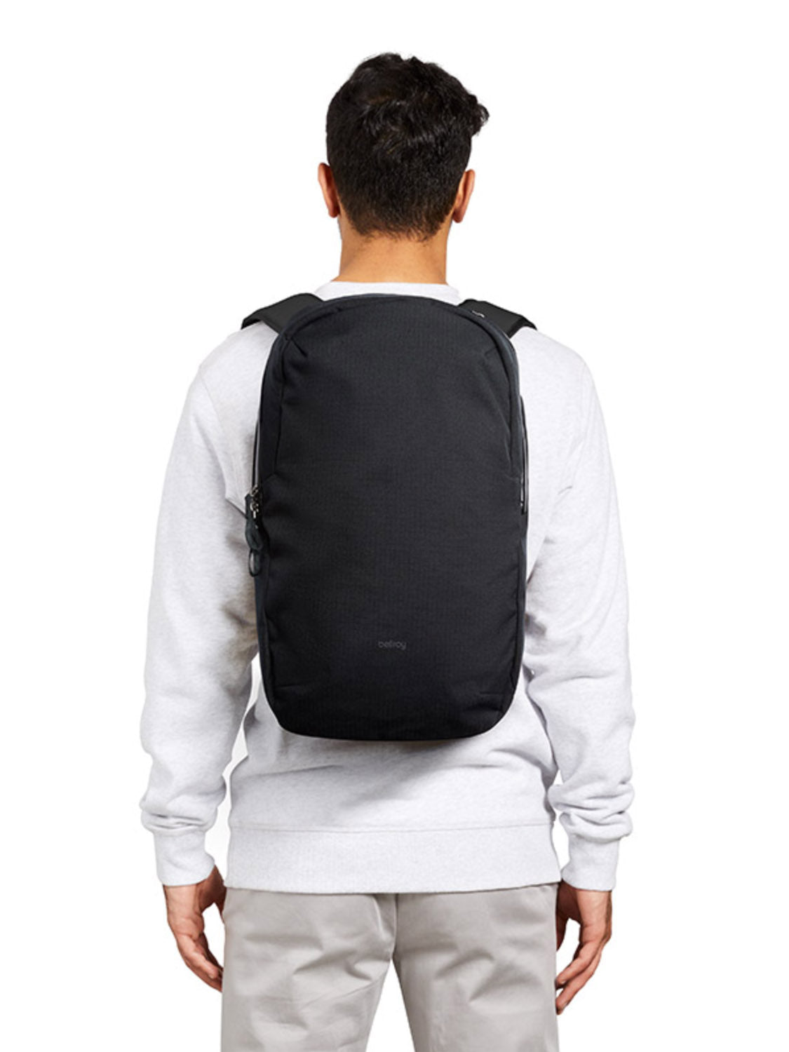A person wearing a light gray sweatshirt and beige pants is seen from behind, carrying the Bellroy Via Backpack - 20L, which features padded shoulder straps and a laptop sleeve.
