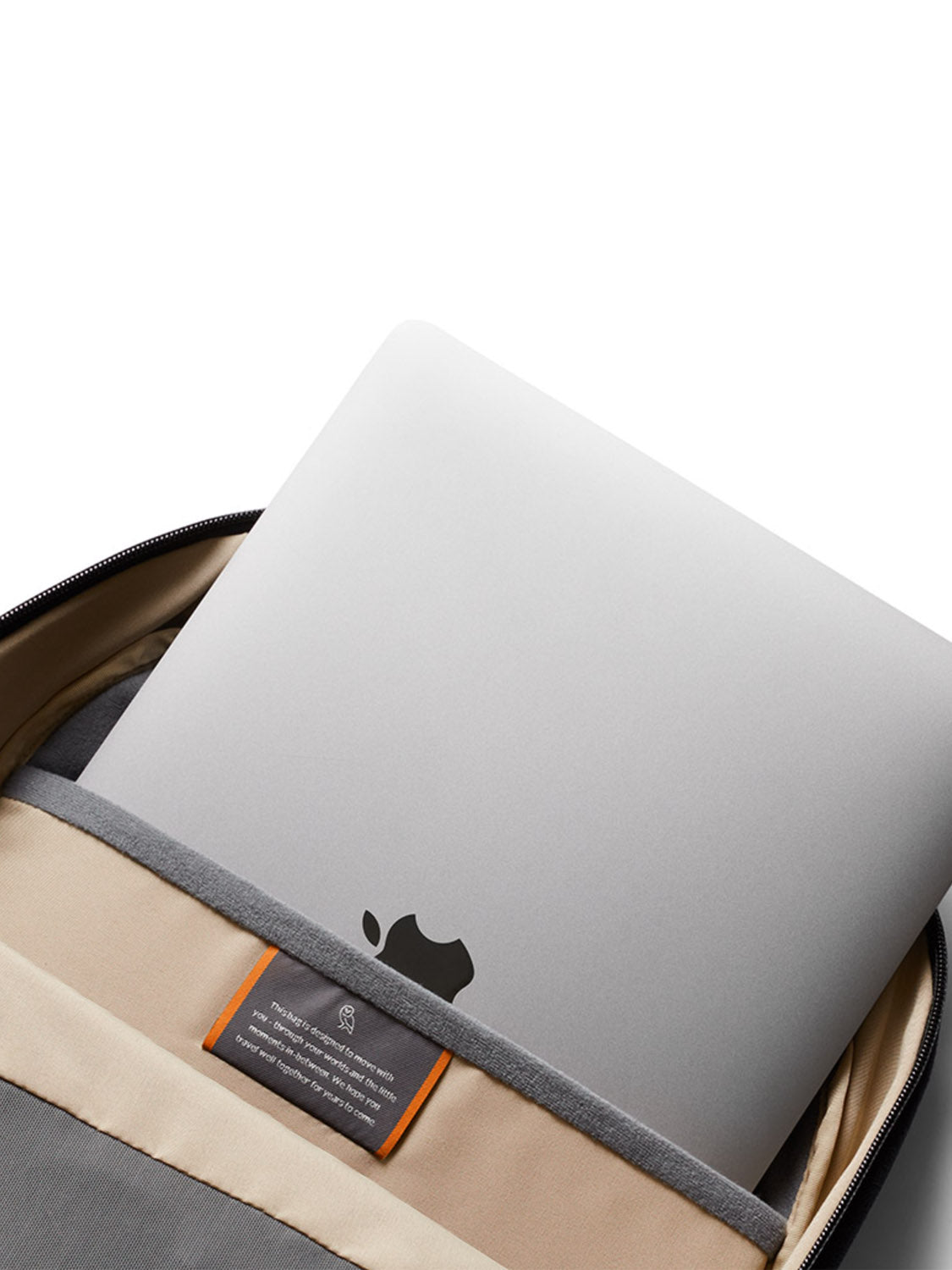 A silver laptop is partially tucked into the Bellroy Via Backpack - 20L, featuring beige and gray recycled fabric, a visible Apple logo, and a small fabric label sewn inside this minimalist backpack.