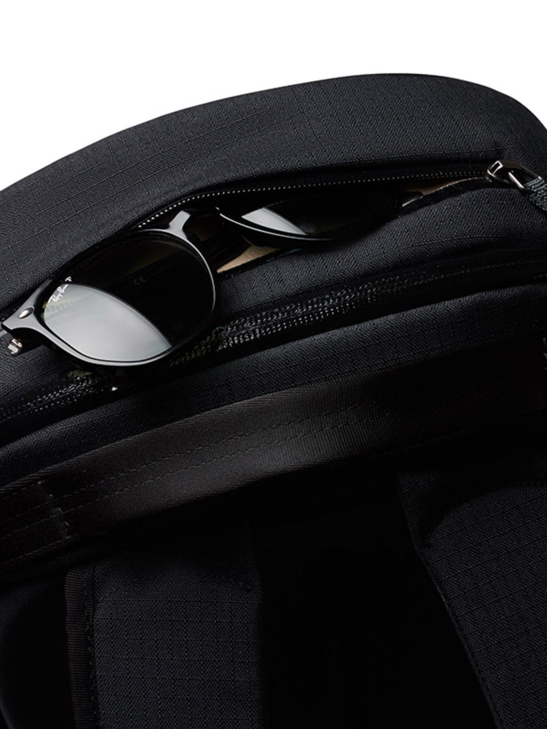 A pair of black sunglasses is partially tucked into the zippered pocket of the Bellroy Via Backpack - 20L, displayed against a white background.