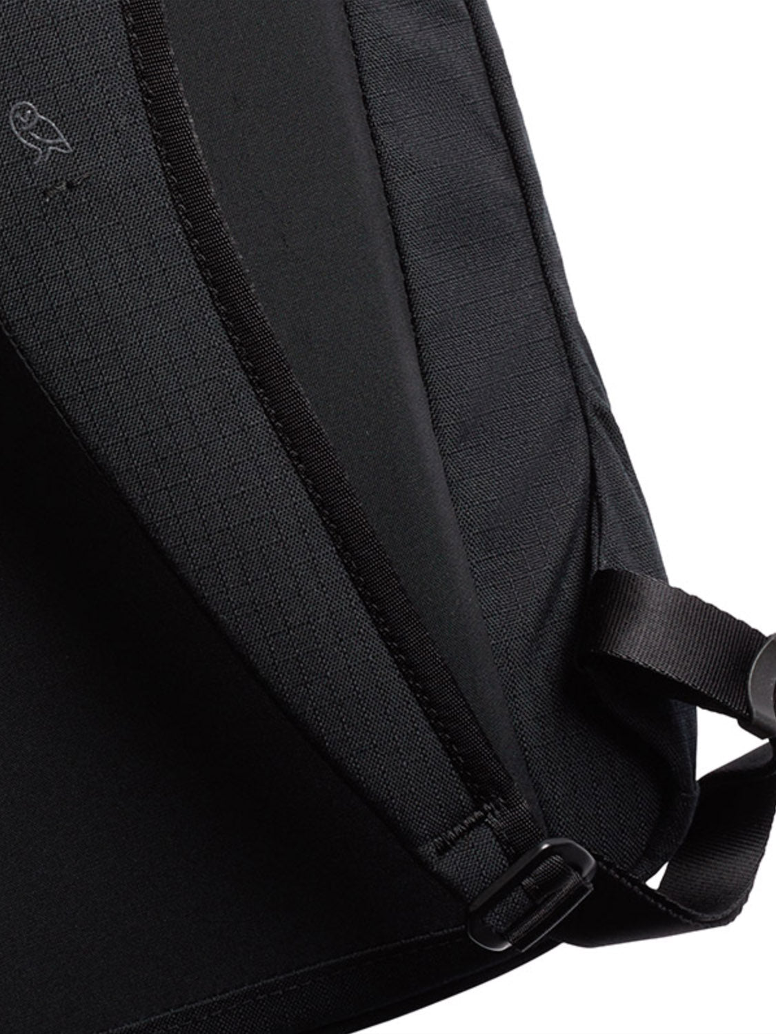 A close-up of Bellroy’s Via Backpack - 20L, made from black recycled fabric with a diagonal seam, strap, small metal buckle, and a subtle embroidered owl logo near the top left corner.