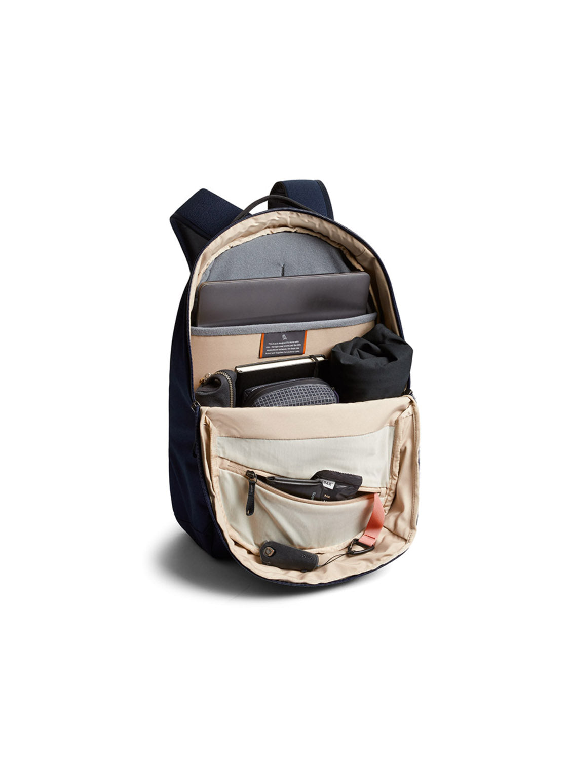 The Bellroy Via Backpack - 20L in navy blue features a beige interior with organized compartments, including a laptop sleeve, tablet slot, space for clothing and accessories. The open front pocket offers easy access to smaller items.