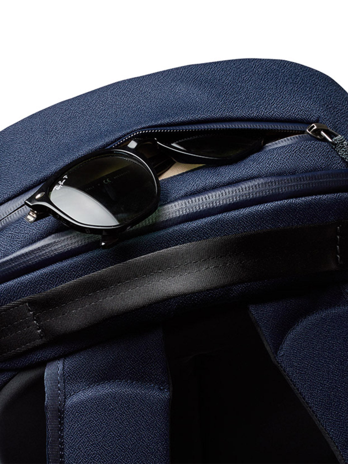 A pair of black sunglasses is partially tucked into the zippered pocket of the Bellroy Via Backpack - 20L, featuring a minimalist design and laptop sleeve, set against a white background.