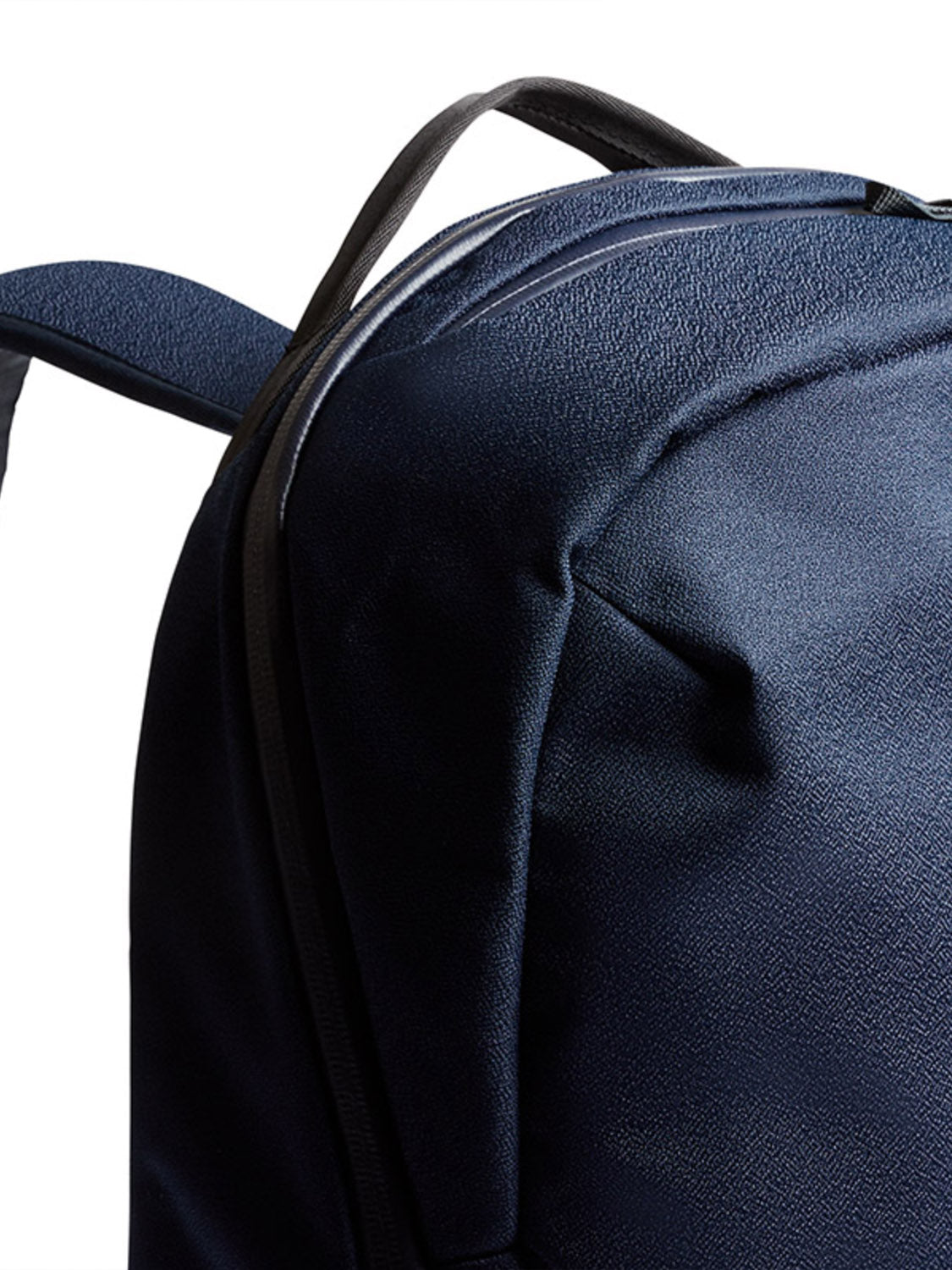 Close-up of the Bellroy Via Backpack - 20L in dark blue, showcasing its textured fabric, top handle, shoulder strap detail, and subtle laptop sleeve against a white background.