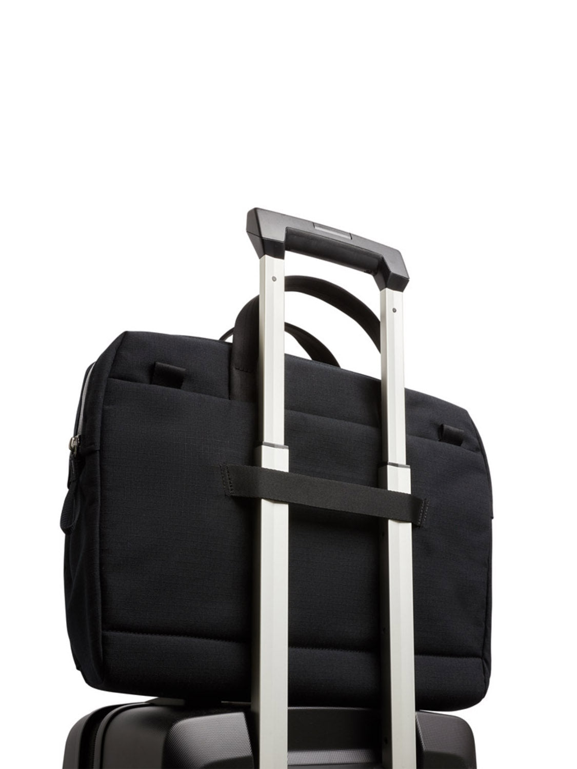 The Bellroy Via Work Bag - 14L, made from recycled fabric in black and featuring a laptop sleeve, is secured atop a suitcase using the telescopic handle, shown against a white background.