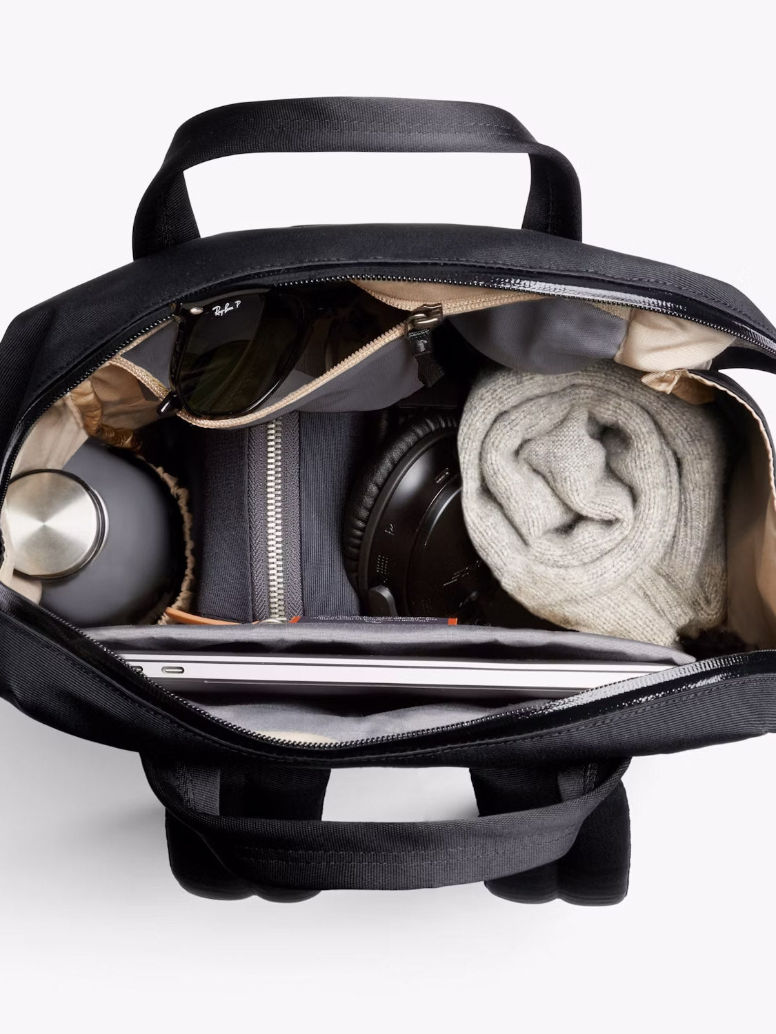 Top-down view of the Bellroy Via Workpack - 18L (black), neatly packed with a water bottle, sunglasses, small zip pouch, large headphones, rolled-up knit sweater, and a laptop in its dedicated compartment.