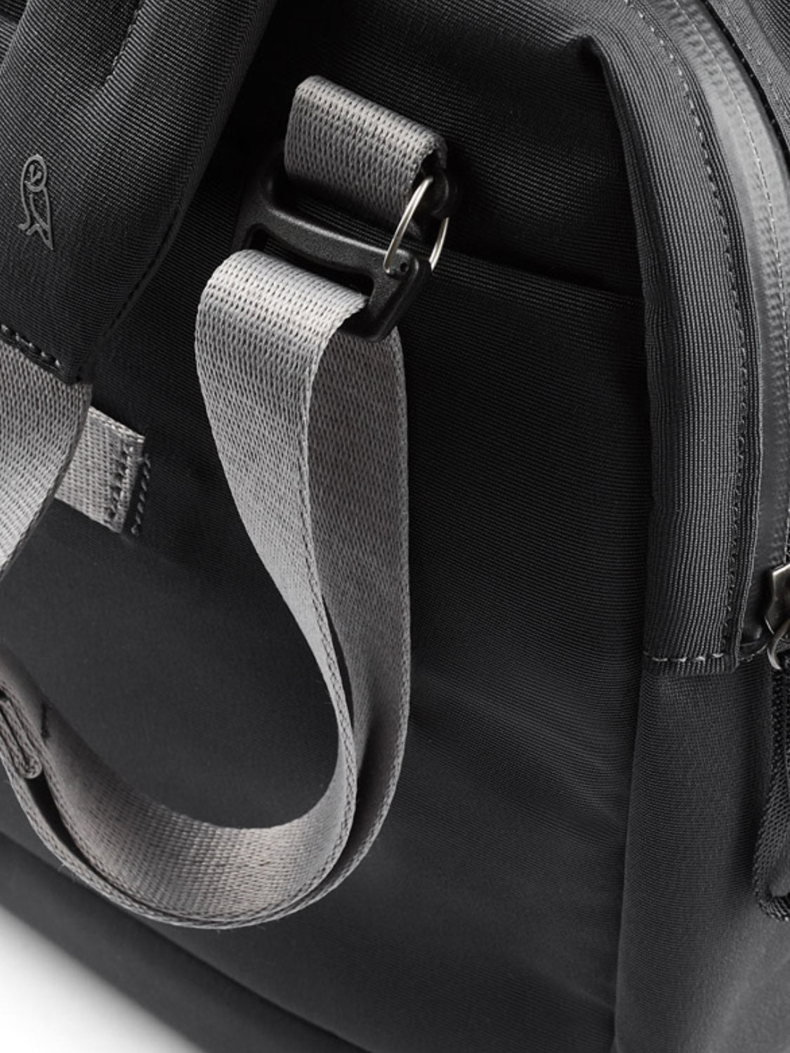 Close-up of the Bellroy Via Work Bag - 14L in black, featuring a grey adjustable strap, metal buckle, visible edge zipper, and durable recycled fabric with detailed stitching for a modern look.