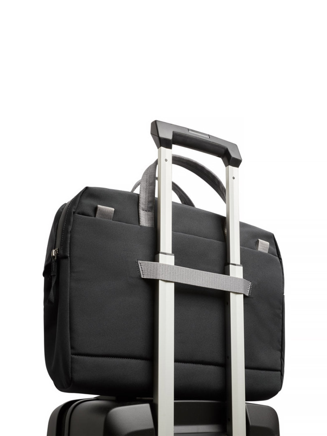 The Bellroy Via Work Bag - 14L in black, featuring a dedicated laptop sleeve, is securely attached to the handle of a rolling suitcase, both set against a plain white background.