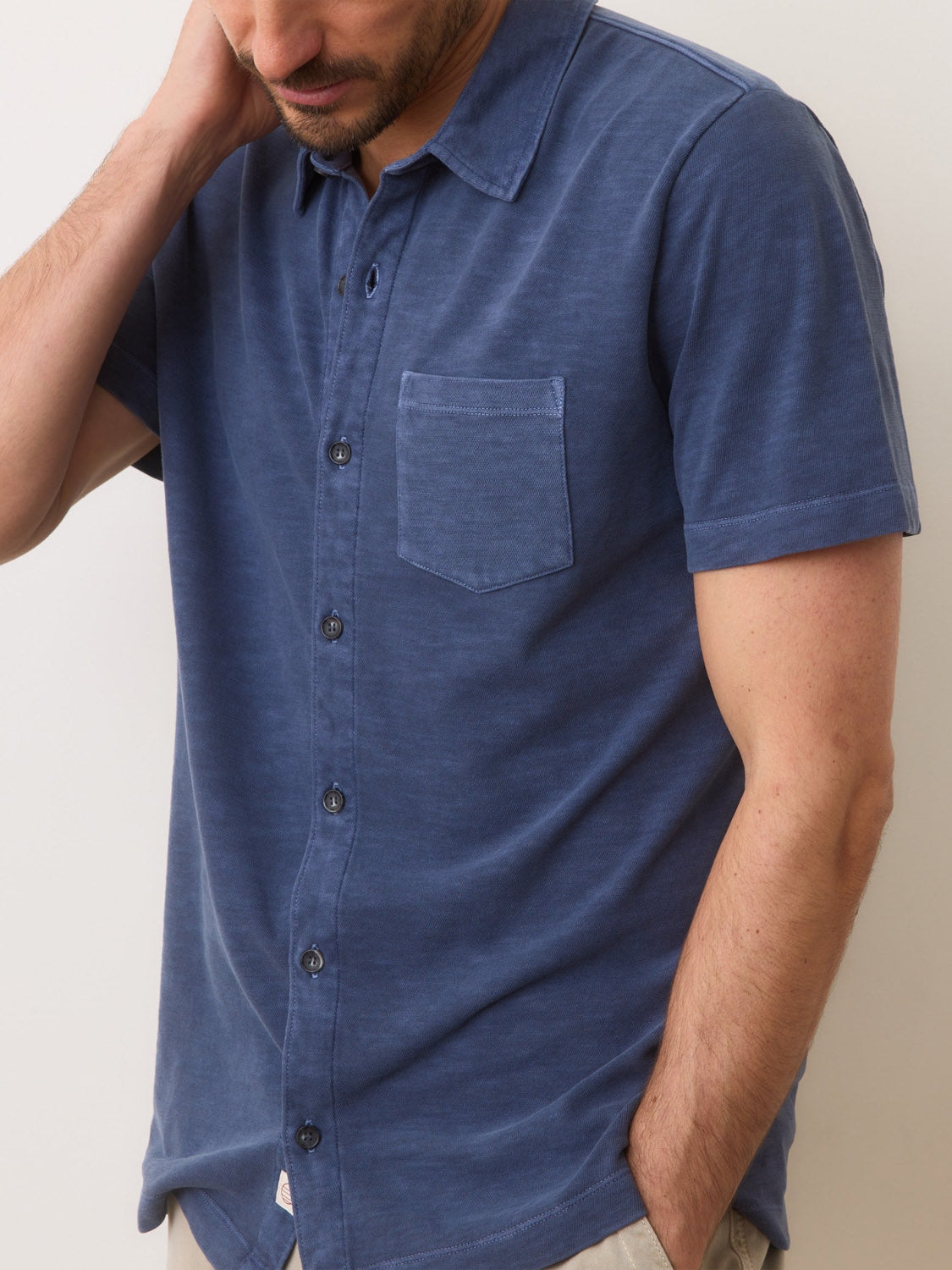 Someone is wearing the Marine Layer Vintage Heavy Slub Button Down in blue, featuring a chest pocket and casual style. Theyre standing with one hand on their neck, partially cropped out of the frame.