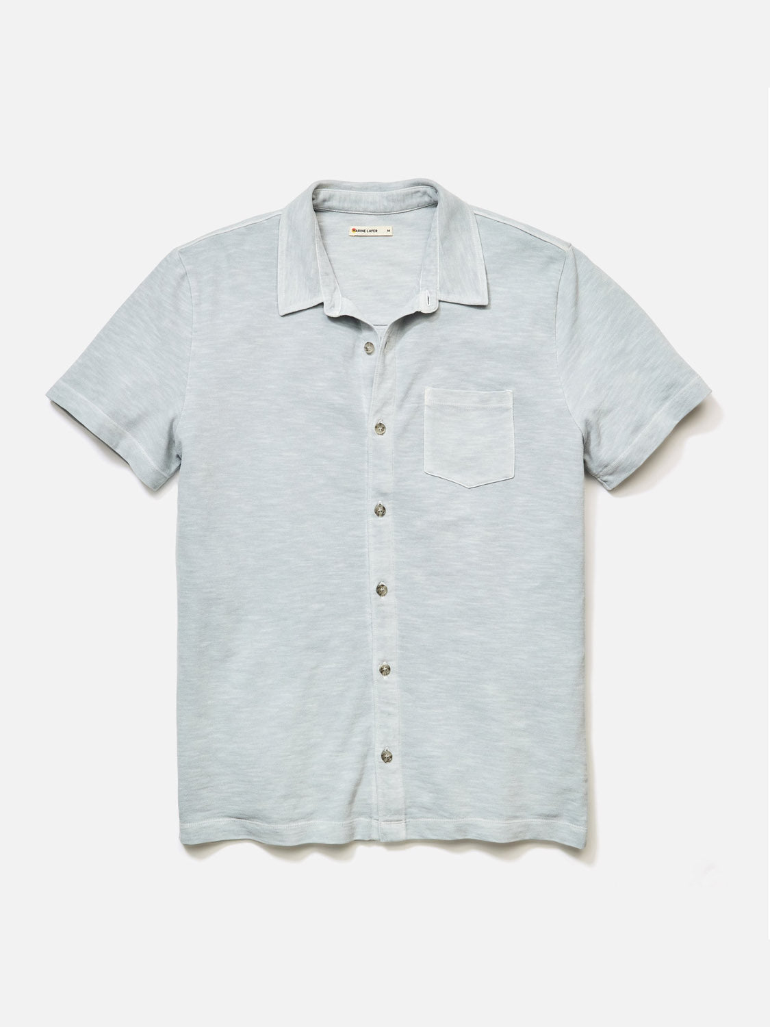 The Marine Layer Vintage Heavy Slub Button Down is a light gray short-sleeve shirt featuring a front pocket, spread collar, and subtle texture, showcased on a plain white background.