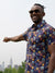 A man in the Viola Printed Cotton Shirt by ID Menswear and sunglasses stands outdoors, smiling as he points toward the Empire State Building on the New York City skyline.