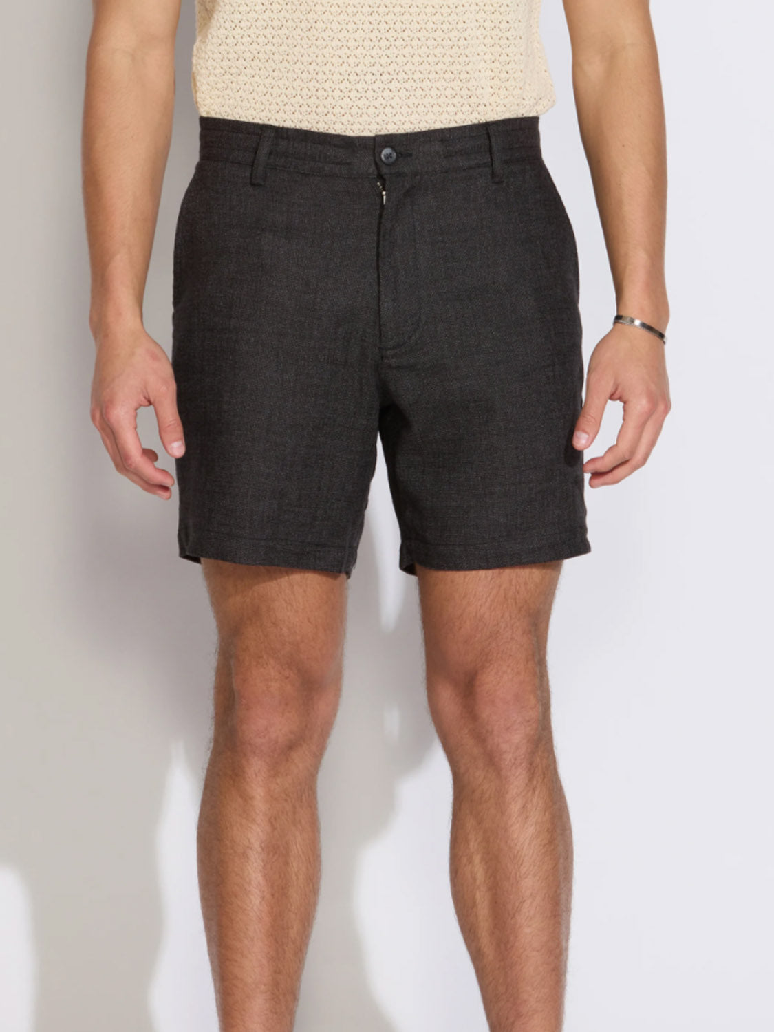 A person wears Civil Society's Vito Relaxed Fit Short in a dark hue with a light patterned short-sleeve shirt, standing against a plain light background. Only the body from shoulders to knees is visible.