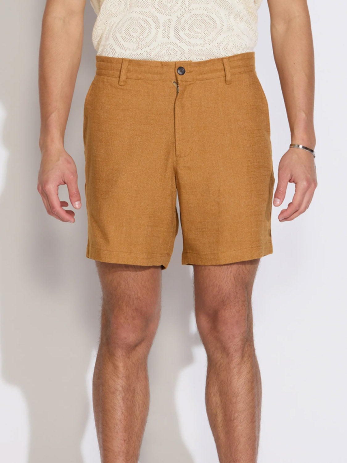A person models Civil Society’s Vito Relaxed Fit Short in light brown linen-blend with button and zipper closure. Only the lower torso and legs are shown against a plain background.