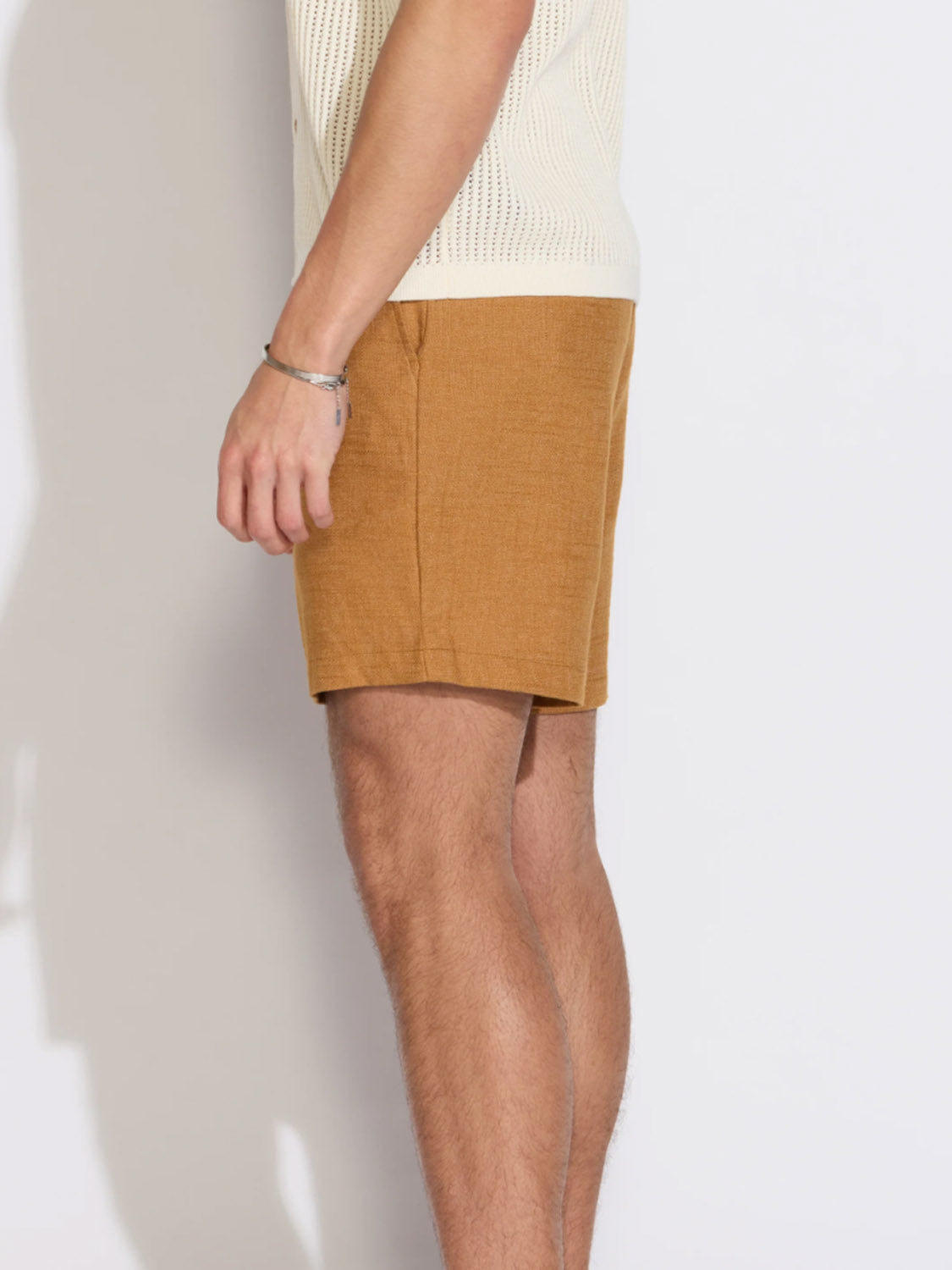 A person is shown from the side against a plain light background, wearing a cream knit top and Civil Society Vito Relaxed Fit Shorts. Only the lower torso and upper legs are visible.