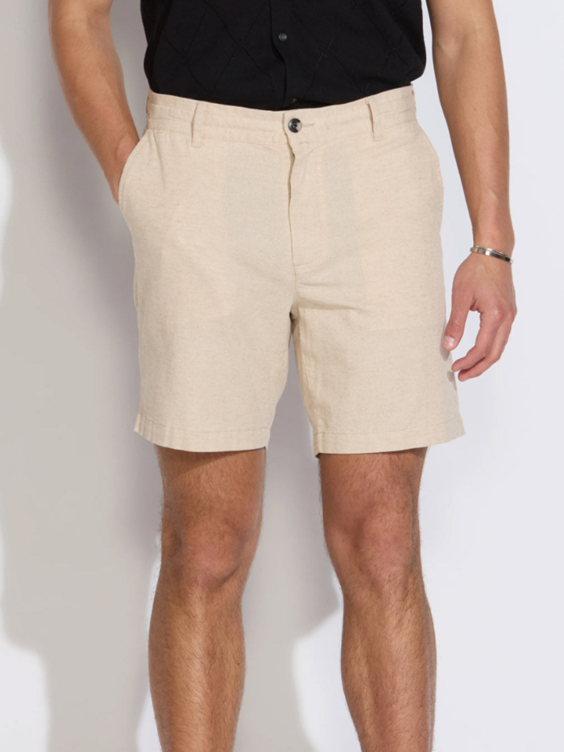 A person wearing Civil Society's Vito Relaxed Fit Short in light beige linen-blend and a black short-sleeve shirt, standing with hands in the shorts' pockets against a plain background.