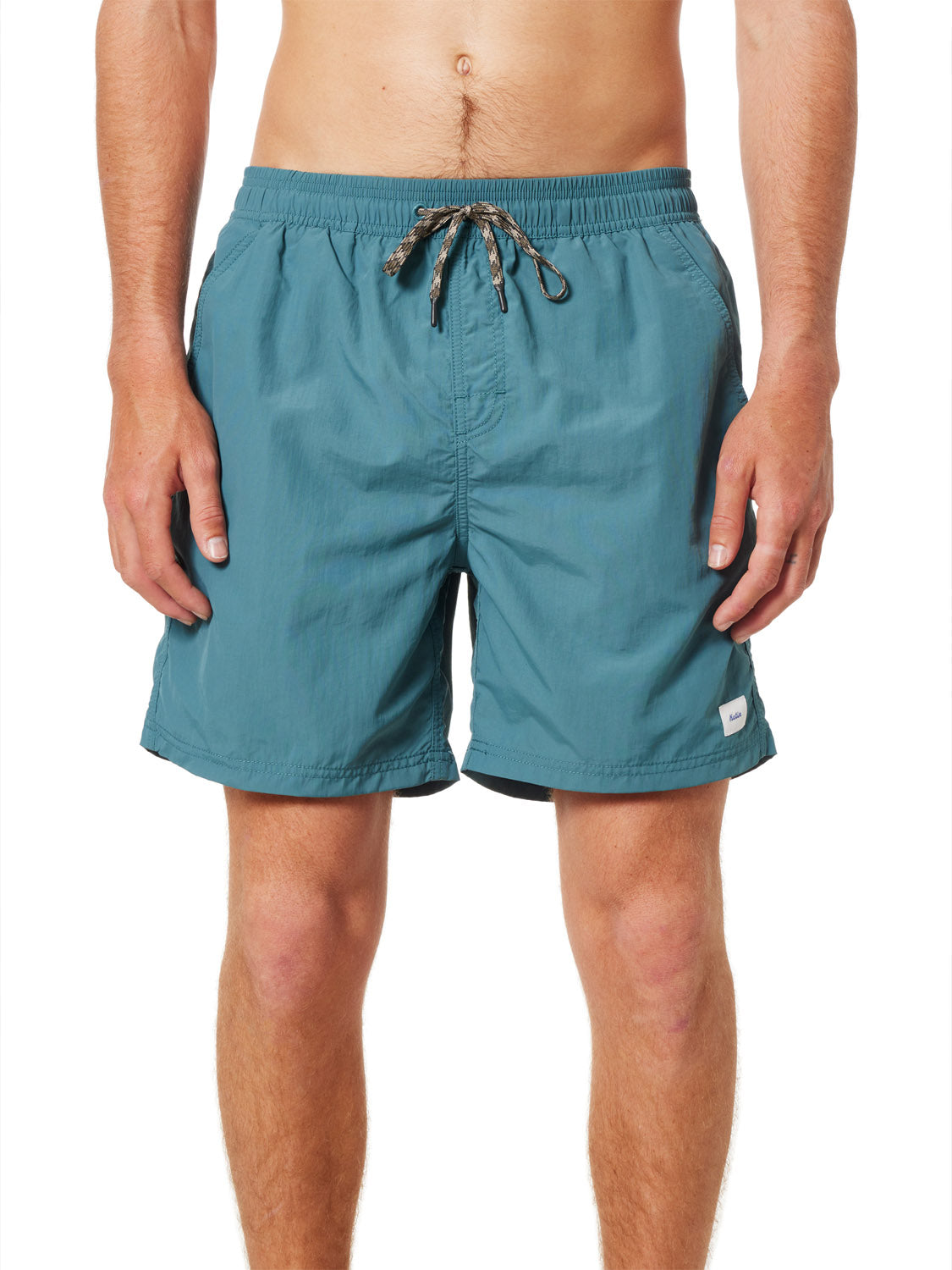 A man models Katin Poolside Volley swim trunks by Katin, featuring a teal color, elastic waistband, mesh brief lining, and a small logo patch near the hem. He stands against a white background with his torso bare and hands at his sides.