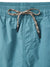 Close-up of Katin Poolside Volley nylon shorts in teal, featuring an elastic waistband and a black-and-tan patterned drawstring tied in a bow at the front. Vertical stitching is visible near the center. Brand: Katin.