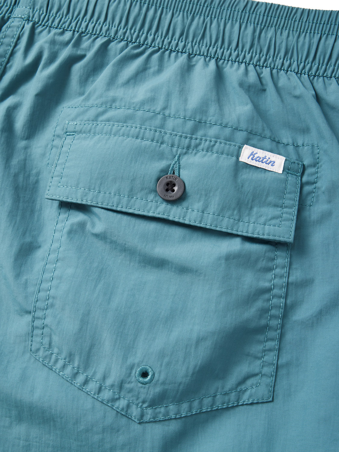 Close-up of the Katin Poolside Volley shorts in teal, made from lightweight nylon with a crinkled texture, an elastic waistband, buttoned back pocket, and small sewn-in Katin label.